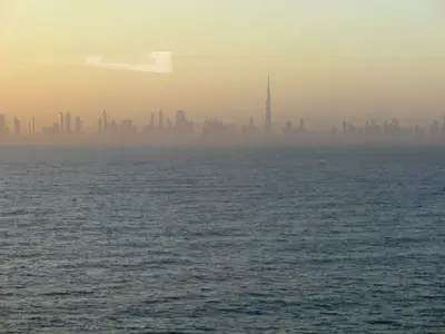 Offene Wasserfläche mit entfernter Silhouette Dubais im Abendlicht